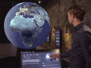 A visitor interacts with a large digital globe displaying real-time environmental data at a media exhibition inside Castle Taggenbrunn.